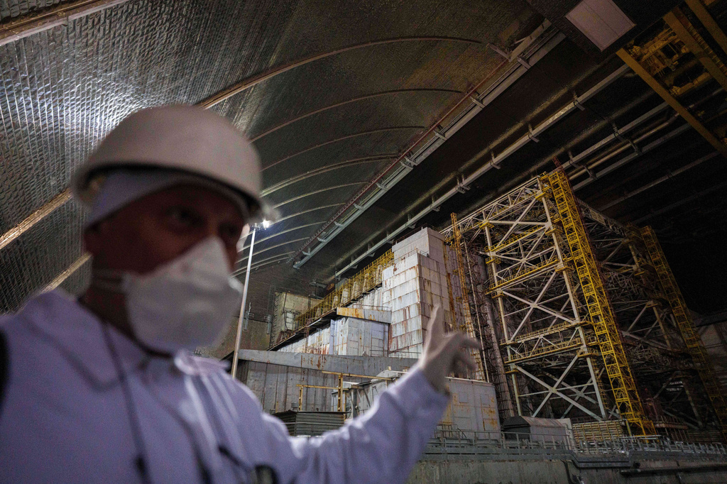A technician of the Chernobyl nuclear power plant in Ukraine stands inside the New Safe Confinement structure and points toward the leaky, Soviet-built “sarcophagus” that covers the damaged reactor on April 6, 2026. (AP Photo/Evgeniy Maloletka)