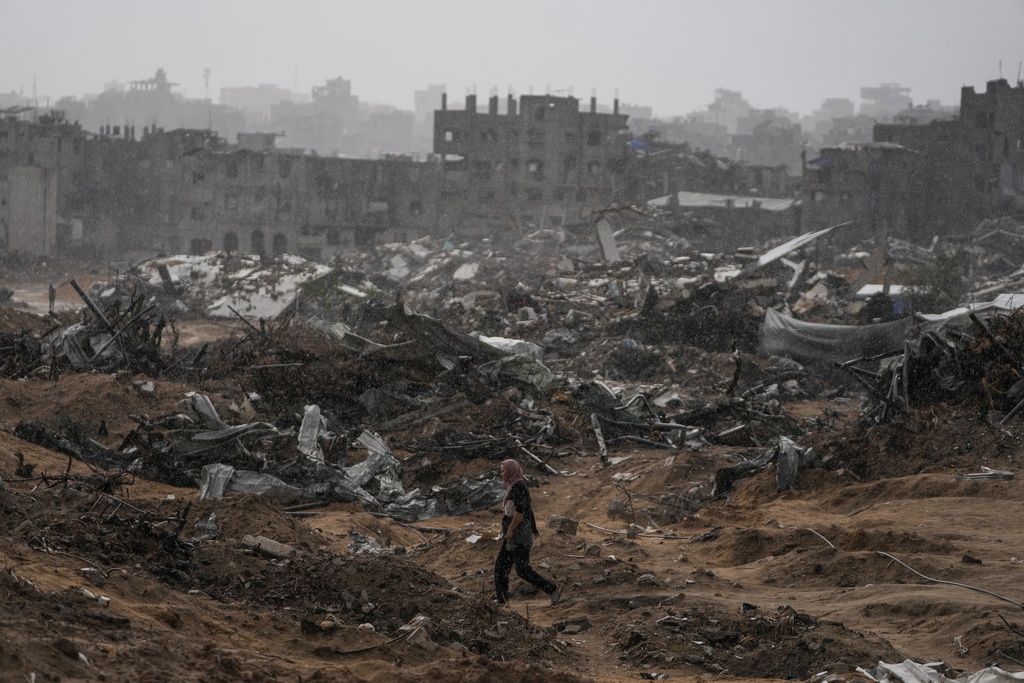 A Palestinian woman walks through a rainstorm past buildings destroyed in Israeli strikes in the Sheikh Radwan neighborhood of Gaza City, Friday, Nov. 14, 2025. (AP Photo/Jehad Alshrafi)