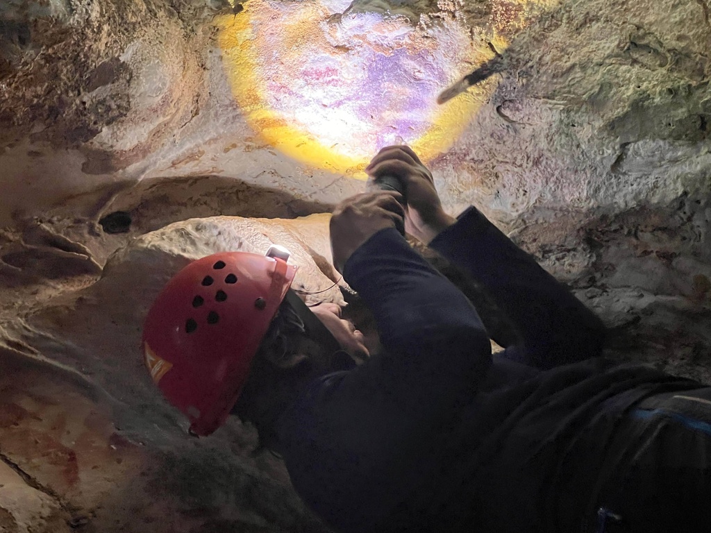 This image provided by Maxime Aubert shows scientist Adhi Agus Oktaviana studying handprints on the walls of a cave in Sulawesi, Indonesia. (Maxime Aubert via AP)