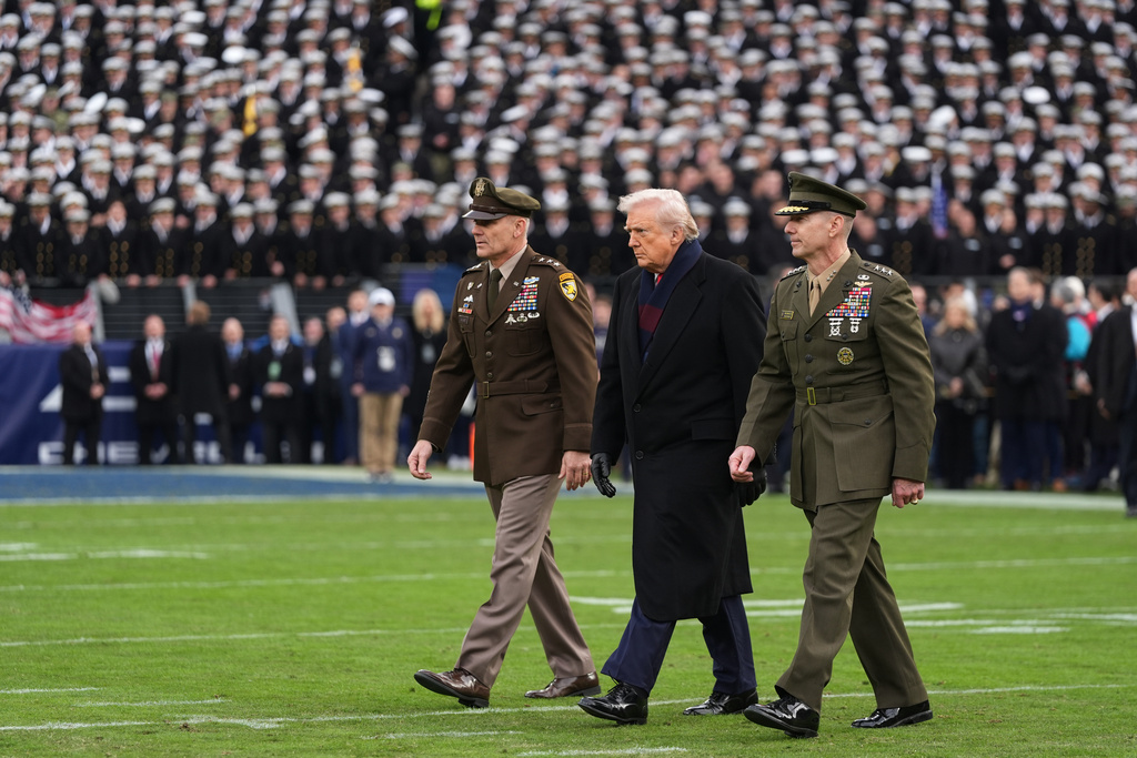 FILE - President Donald Trump is escorted on to the field to take part in the ceremonial coin toss before the start of the NCAA college football game between Army and Navy at M&T Bank Stadium in Baltimore, Saturday, Dec. 13, 2025. (AP Photo/Stephanie Scarbrough, File)