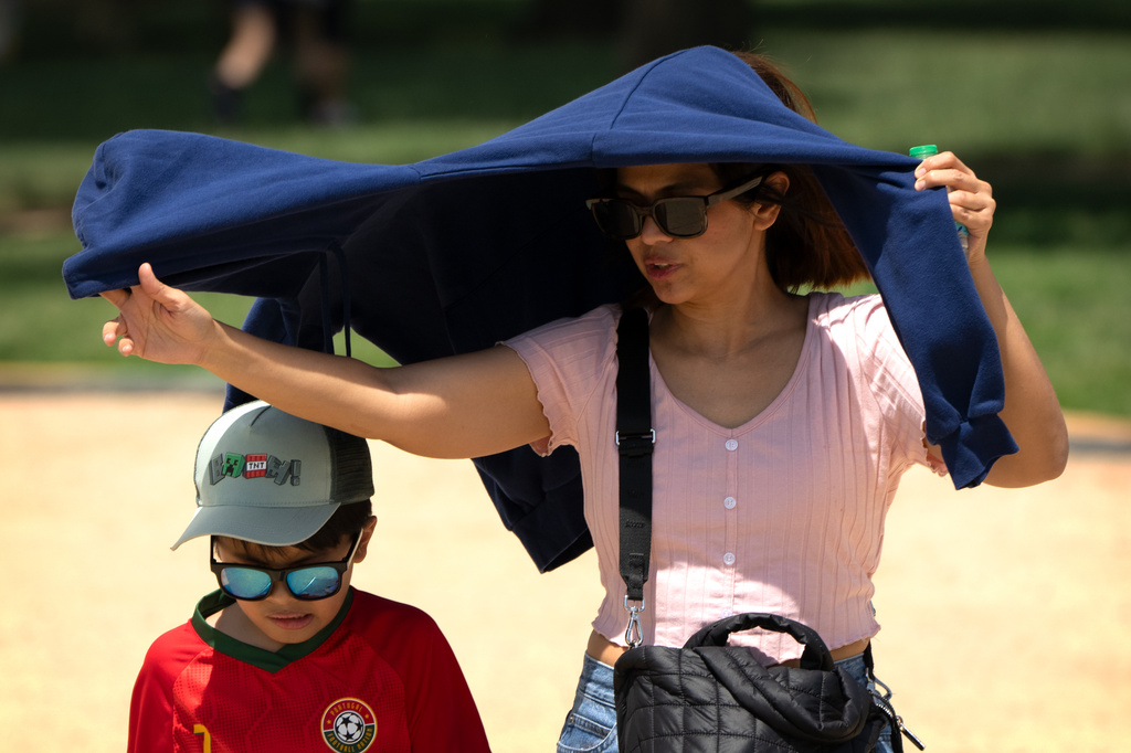Visitors use a jacket for shade as they walk at the Great American State Fair on the National Mall, Tuesday, June 30, 2026, in Washington. (AP Photo/Mark Schiefelbein)