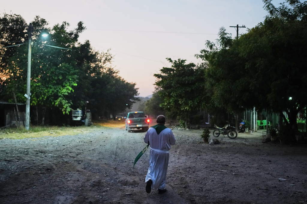 Rev. Gilberto Vergara walk toward a house to blesses a person in Apatzingan in the Michoacan state of Mexico, Wednesday, Nov. 19, 2025. (AP Photo/Eduardo Verdugo)