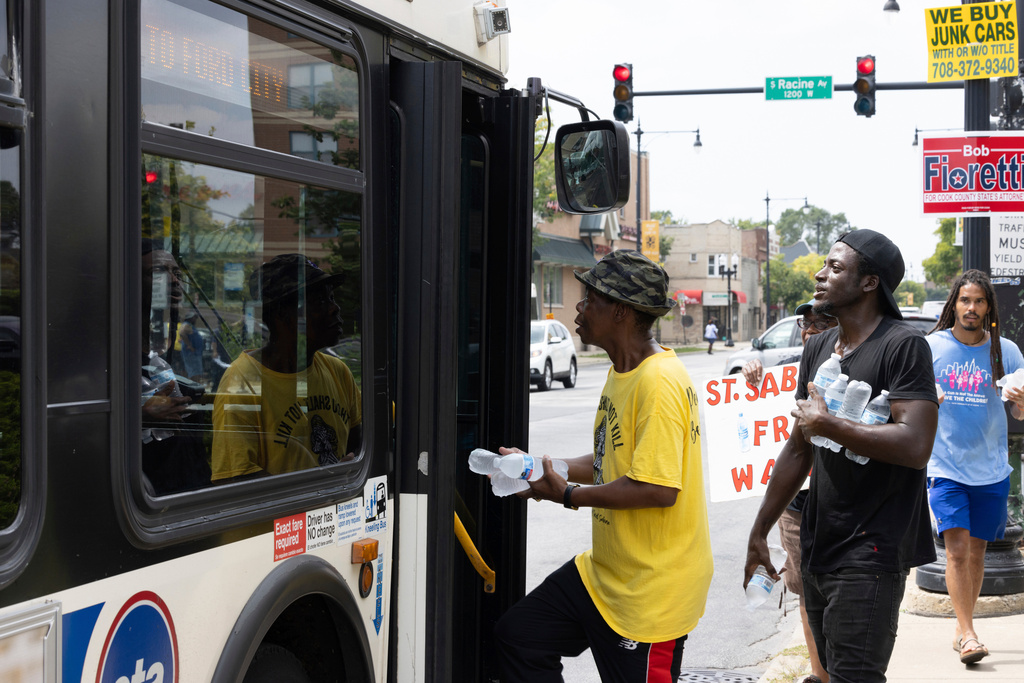 FILE - Volunteers from Saint Sabina Church climb aboard a bus to distribute bottles of cold water at a busy South Side intersection in Chicago, Aug. 27, 2024. (AP Photo/Teresa Crawford, File)
