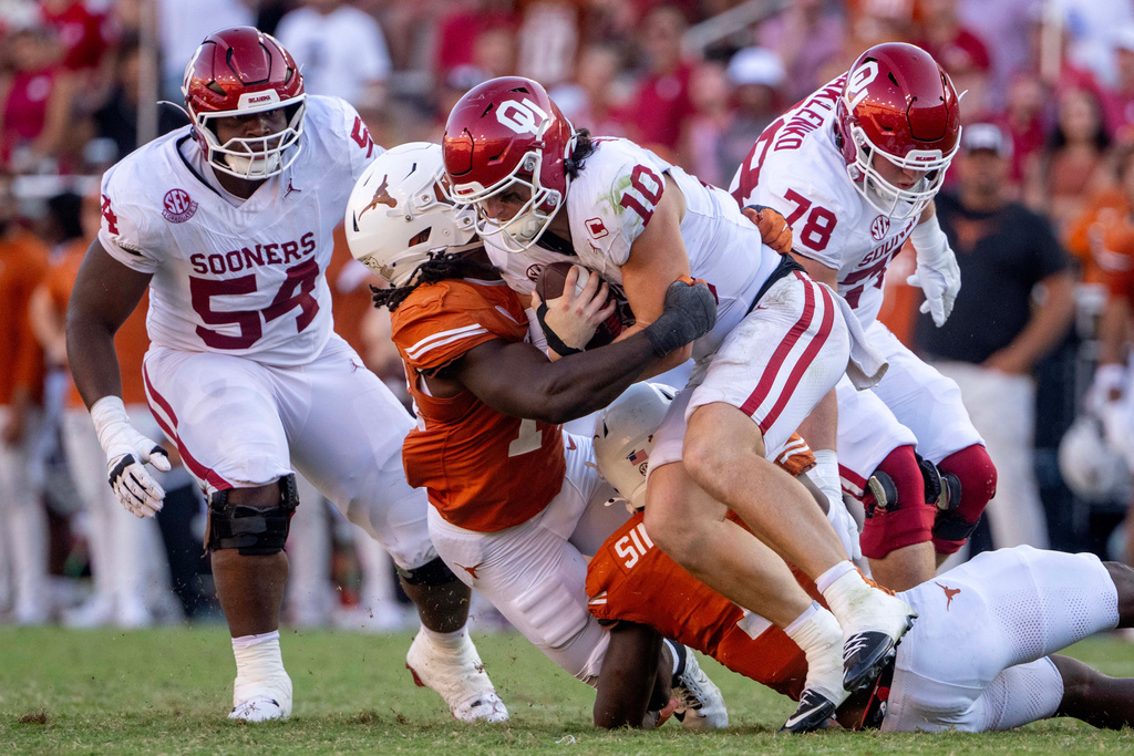 Oklahoma quarterback John Mateer (10) is sacked by Texas defensive end Brad Spence, center left, and defensive end Colin Simmons, bottom right, during the second half of an NCAA college football game Saturday, Oct. 11, 2025, in Dallas. (AP Photo/Jeffrey McWhorter)