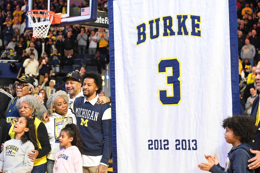 Former Michigan basketball player Trey Burke, center left, reacts as a banner of his jersey number is prepared to be raised to the Crisler Center rafters during halftime of an NCAA college basketball game against Ohio State, Friday, Jan. 23, 2026, in Ann Arbor, Mich. (AP Photo/Jose Juarez)