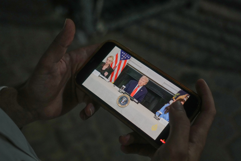 Palestinian paramedic Saeed Awad looks at his phone displaying an image of U.S. President Donald Trump, following the announcement that Israel and Hamas have agreed to the first phase of a peace plan to pause fighting, as he stands at Al-Aqsa Hospital, in Deir al-Balah, in the central Gaza Strip, Thursday, Oct. 9, 2025. (AP Photo/Abdel Kareem Hana)
