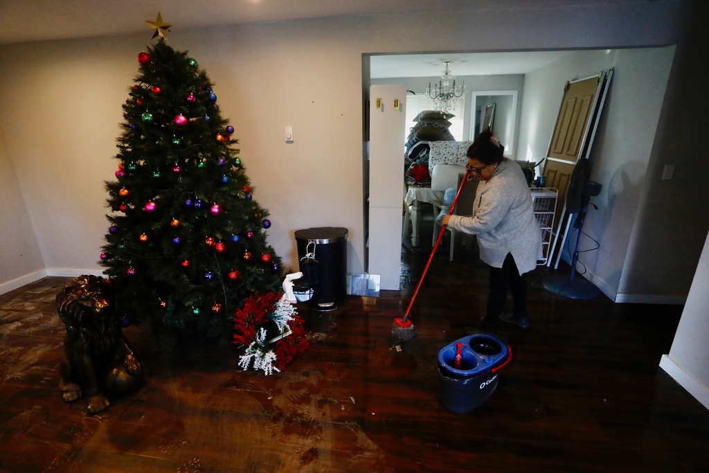Francis Tarango mops inside her daughters' home damaged by floodwaters in Burlington, Wash., Saturday, Dec. 13, 2025. (AP Photo/Manuel Valdes)
