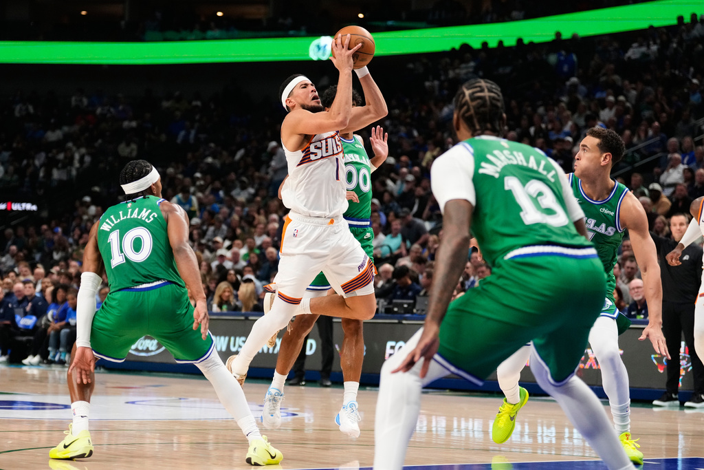 Phoenix Suns' Devin Booker (1) shoots as Dallas Mavericks' Brandon Williams (10), Max Christie (00) and Naji Marshall (13) defend in the first half of an NBA basketball game Wednesday,Nov. 12, 2025, in Dallas. (AP Photo/Tony Gutierrez)