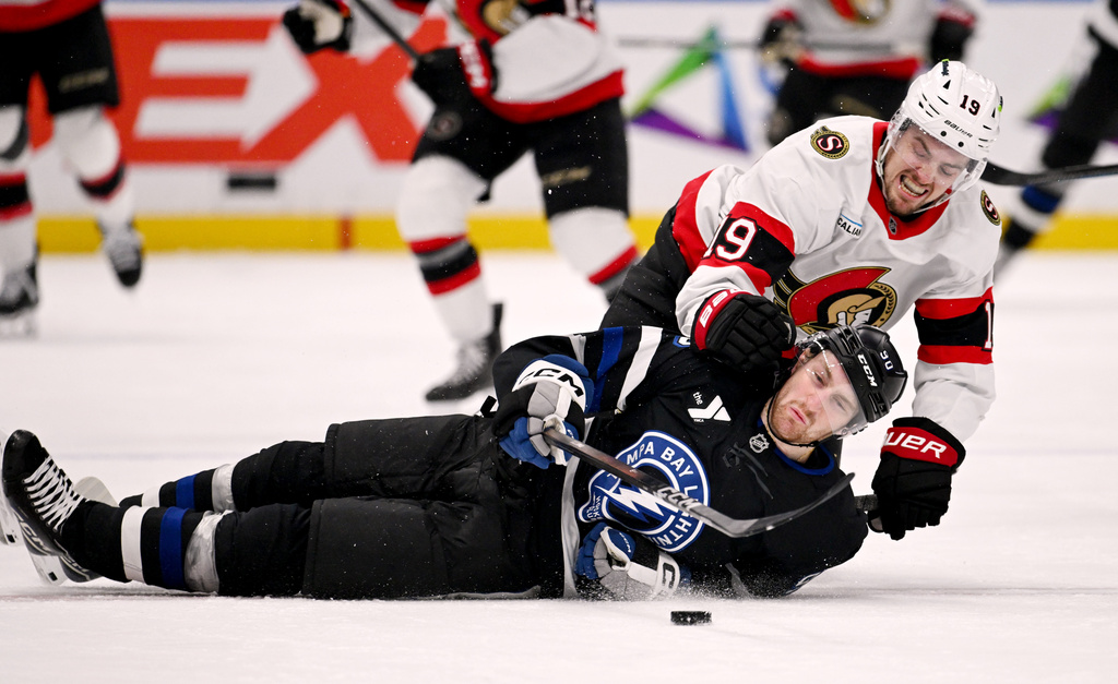 Tampa Bay Lightning defenseman J.J. Moser (90) is pulled down to the ice by Ottawa Senators right wing Drake Batherson (19) as they battle for the puck during the first period of an NHL hockey game Saturday, March 28, 2026, in Tampa, Fla. (AP Photo/Jason Behnken)