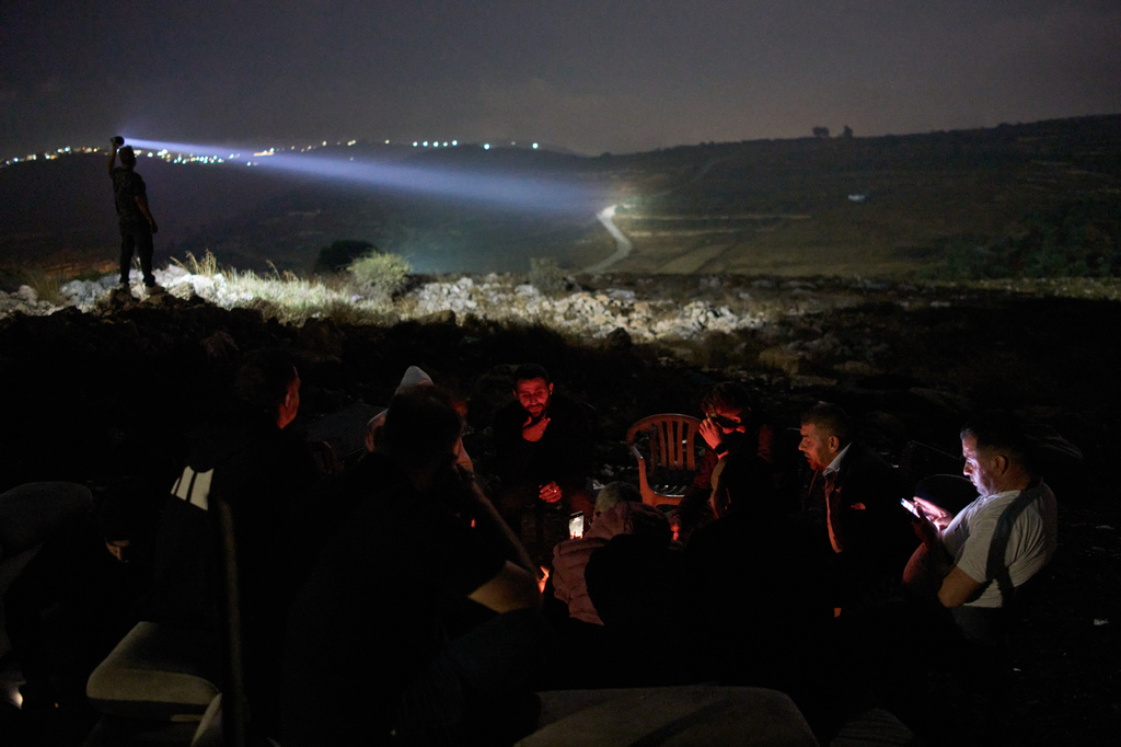 Palestinians gather around a bonfire as a volunteer scans a valley with a flashlight during a night watch to help prevent Israeli settler attacks in the West Bank town of Sinjil, Monday, July 27, 2026. Nightly watches have become a part of daily life, with no government or security force willing to protect them. (AP Photo/Leo Correa)
