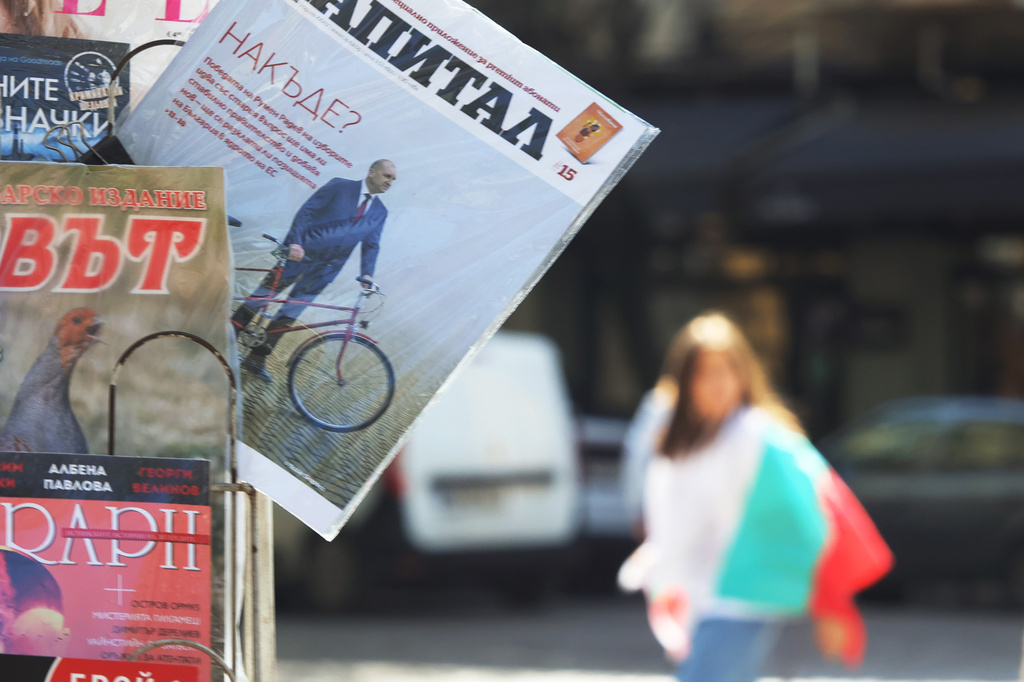 A person carrying Bulgarian Flag passes behind newspaper's cover showing the Former President Rumen Radev under a title "Where to from here?" In Sofia, Monday, April 20, 2026. (AP Photo/Valentina Petrova)