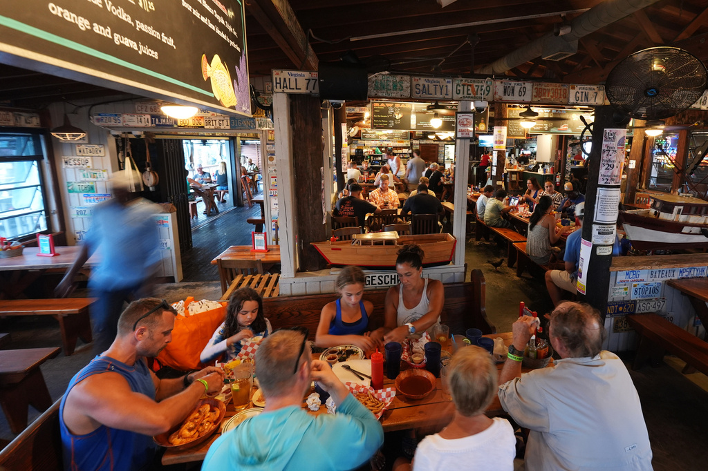 An employee bussing tables, left, walks past diners as he works inside Half Shell Raw Bar, Friday, July 24, 2026, in Key West, Fla. (AP Photo/Rebecca Blackwell)