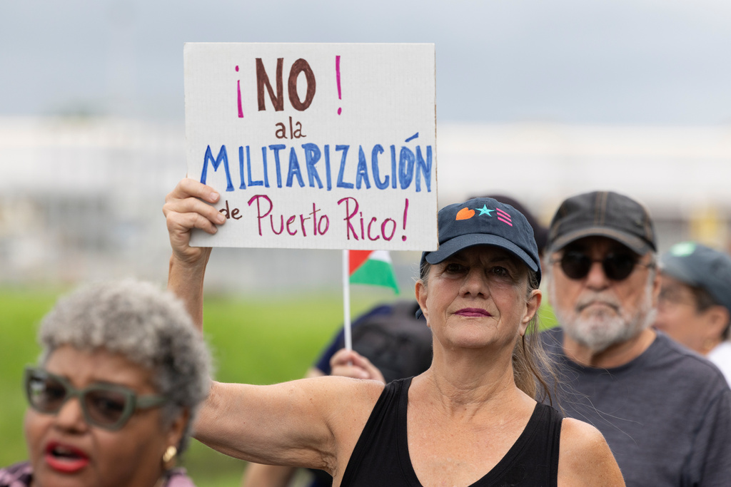 A demonstrator holds a sign that reads in Spanish, "No to the militarization of Puerto Rico" during a protest outside the Muñiz Air National Guard Base in Carolina, Puerto Rico, Sunday, Sept. 7, 2025. (AP Photo/Alejandro Granadillo)