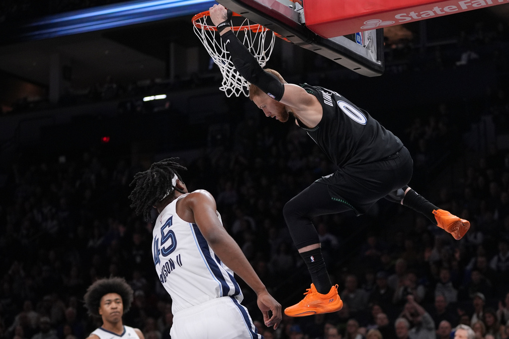Minnesota Timberwolves guard Donte DiVincenzo (0) hangs on the rim next to Memphis Grizzlies forward GG Jackson (45) after a dunk during the first half of an NBA basketball game, Tuesday, March 3, 2026, in Minneapolis. (AP Photo/Abbie Parr)