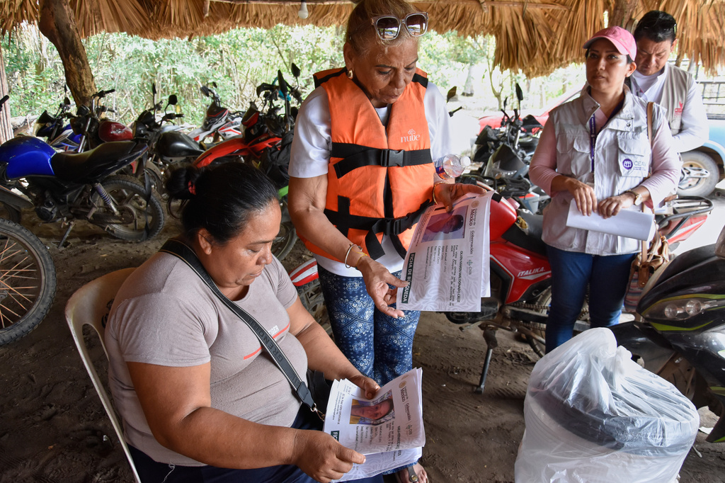 Julia Margarita Bravo Diaz, of Cuba, wearing life jacket, shows photos of missing people, including her daughter Meiling Álvarez Bravo and grandson Samei Armando Reyes Álvarez, to local residents in San Jose Hueyate, Chiapas state, Mexico, Saturday, May 9, 2026, during a search for migrants who vanished in late 2024 along a maritime smuggling route to the U.S. (AP Photo/Edgar H. Clemente)