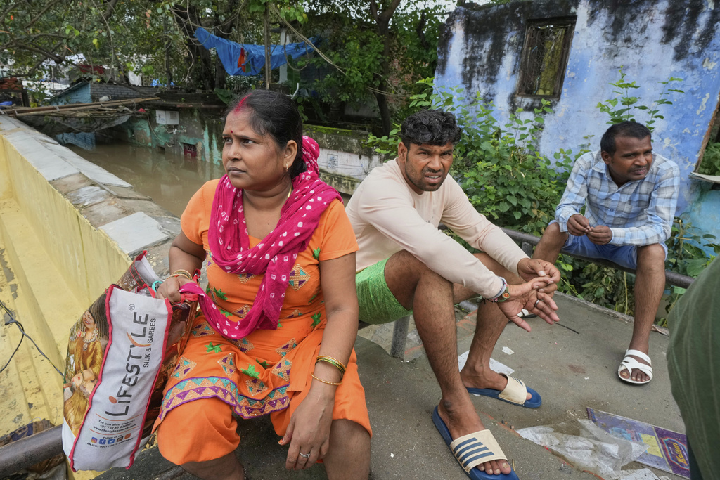 Bindu Pandey, 40, left, sits on the wall near the floodwaters of the swollen Yamuna River, leaving behind her inundated home on the banks to seek refuge in a temporary shelter, in New Delhi, India, Friday, Sept. 5, 2025. (AP Photo/Manish Swarup)