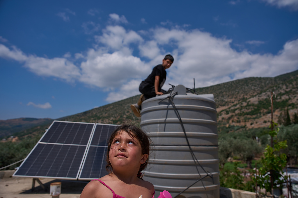 A girl looks toward what residents said was an Israeli drone flying overhead as a boy checks his family's water storage tank in Halta, southern Lebanon, Friday, June 12, 2026. (AP Photo/Hassan Ammar)