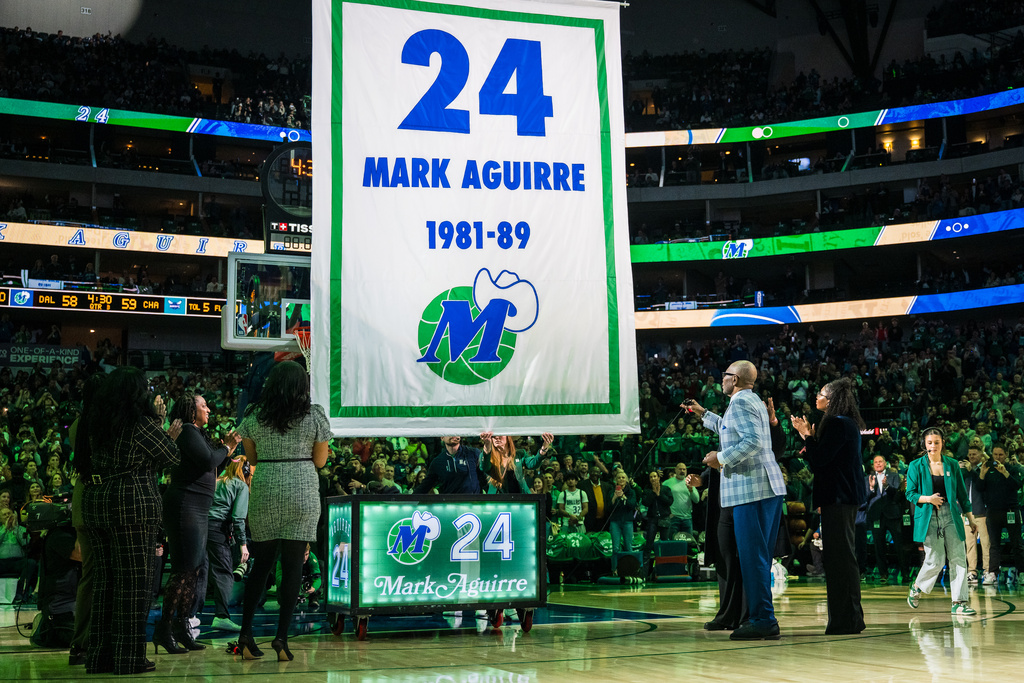 Former Dallas Mavericks player Mark Aguirre, second from front right, is joined by family as a banner is raised during his jersey retirement presentation at halftime during an NBA basketball game between the Mavericks and the Charlotte Hornets, Thursday, Jan. 29, 2026, in Dallas. (AP Photo/Jessica Tobias)