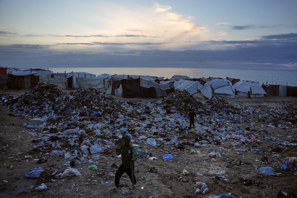 Children walk over a pile of garbage at a makeshift tent camp for displaced Palestinians on a beach in Deir al-Balah, in the Gaza Strip Friday, Jan. 16, 2026. (AP Photo/Abdel Kareem Hana)