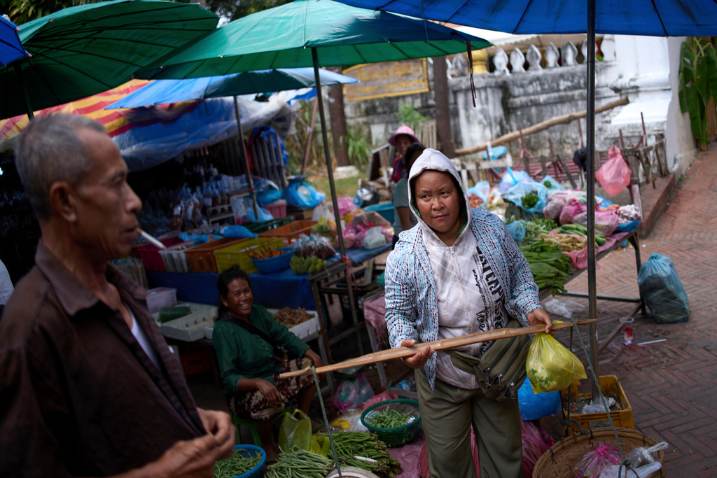 A vendor carries fresh produce with a shoulder pole through the bustling post-dawn morning market in Luang Prabang, Laos, as local residents shop for daily necessities, Sunday, Nov. 2, 2025. (AP Photo/Eugene Hoshiko)