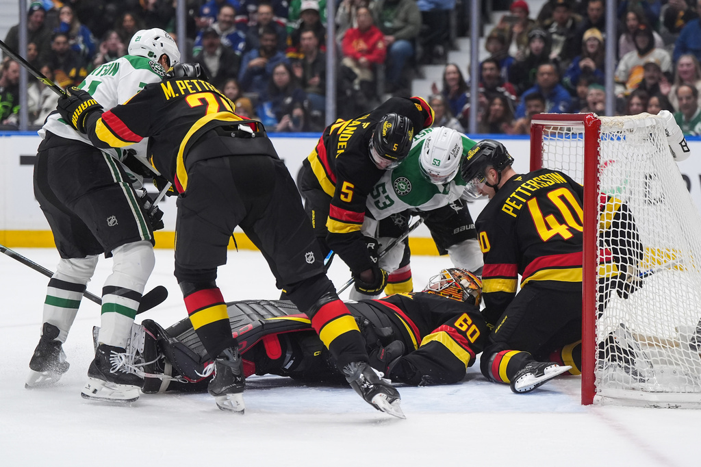 Vancouver Canucks goalie Nikita Tolopilo (60) lies on the puck as teammates Elias Pettersson (40), Tom Willander (5) and Marcus Pettersson (29) defend against Dallas Stars' Wyatt Johnston (53) and Jason Robertson (21), left, during the first period of an NHL hockey game in Vancouver, British Columbia, Monday, March 2, 2026. (Darryl Dyck/The Canadian Press via AP)