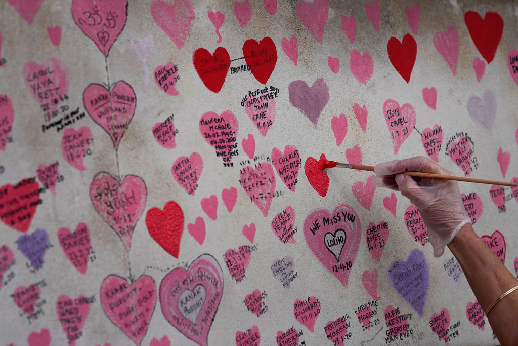 FILE - A volunteer re-paints a faded heart on the COVID-19 memorial wall in Westminster in London, Friday, Oct. 15, 2021. (AP Photo/Kirsty Wigglesworth, File)