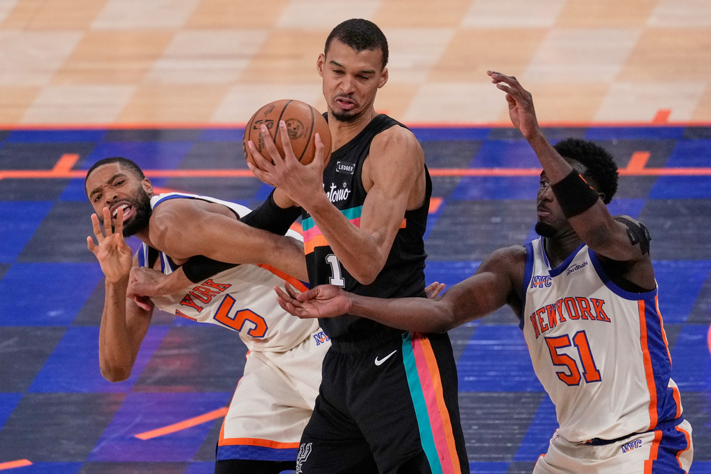 New York Knicks' Mikal Bridges, left, fouls San Antonio Spurs' Victor Wembanyama, center, while Bridges and Mohamed Diawara (51) try to get to the ball during the second half of an NBA basketball game Sunday, March 1, 2026, in New York. (AP Photo/Seth Wenig)