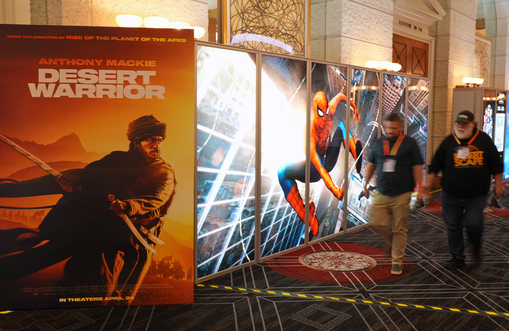 CinemaCon attendees walk past advertisements for upcoming films including "Desert Warrior" and "Spiderman: Brand New Day" during the opening day of CinemaCon 2026, the official convention of Cinema United, on Monday, April 13, 2026, at Caesars Palace in Las Vegas. (AP Photo/Chris Pizzello)