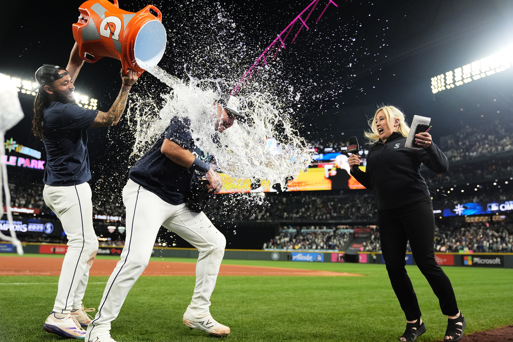 Seattle Mariners' Cal Raleigh, center, is dunked during a post game interview by shortstop J.P. Crawford after the team's win against the Colorado Rockies to win the American League West Division, Wednesday, Sept. 24, 2025, in Seattle. (AP Photo/Ryan Sun)