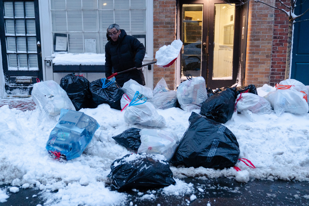 Key Lim, 55, of Quincy, removes snow from a sidewalk lined with trash bags in front of the laundromat that he manages on Tuesday, Feb. 24, 2026, in Boston. (AP Photo/Sophie Park)