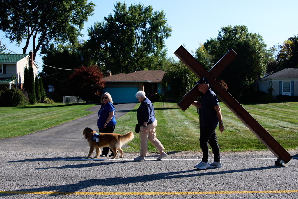 Dan Beazley, of Northville, carries a homemade cross past a therapy dog to The Church of Jesus Christ of Latter-day Saints in Grand Blanc Township, Mich., Tuesday, Sept. 30, 2025, after a man rammed his vehicle into the building before opening fire and setting the building ablaze Sunday morning. (AP Photo/Ryan Sun)