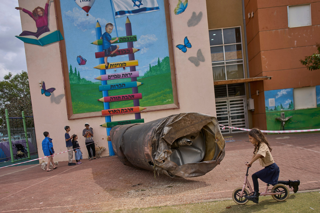 Children play beside a fragment of an Iranian ballistic missile that landed in a schoolyard in the Israeli settlement of Peduel in the West Bank Monday, March 23, 2026. (AP Photo/Ohad Zwigenberg)