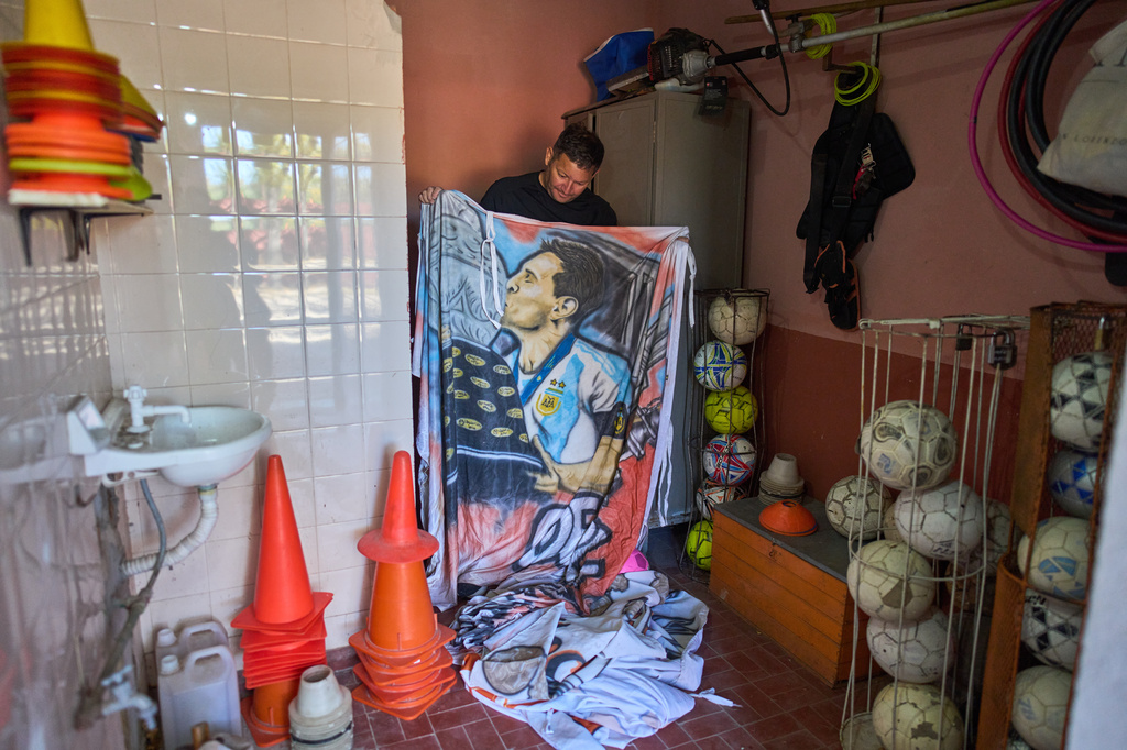 Worker Jorge Sosa holds a flag, kept in a locker room at the Grandoli club, features soccer star Lionel Messi to be hung next to the pitch before the start of children's matches in Rosario, Argentina, Saturday, May 2, 2026. (AP Photo/Rodrigo Abd)