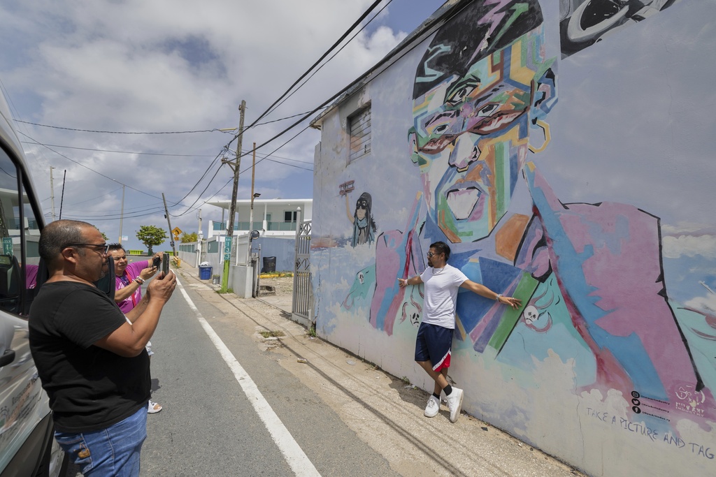 A visitor on a guided tour poses for photos in front of a mural of Bad Bunny at Playa Puerto Nuevo in Vega Baja, Puerto Rico, Tuesday, Aug. 12, 2025. (AP Photo/Alejandro Granadillo)