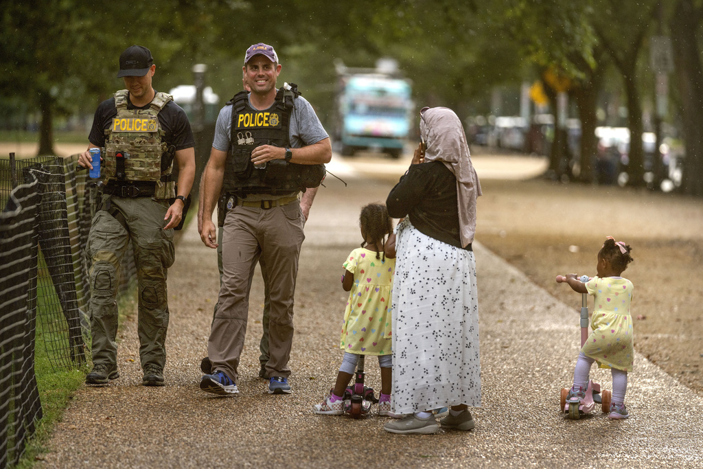 A woman and children watch as officers with the Drug Enforcement Administration patrol along the National Mall Wednesday, Aug. 13, 2025, in Washington. (AP Photo/Mark Schiefelbein)