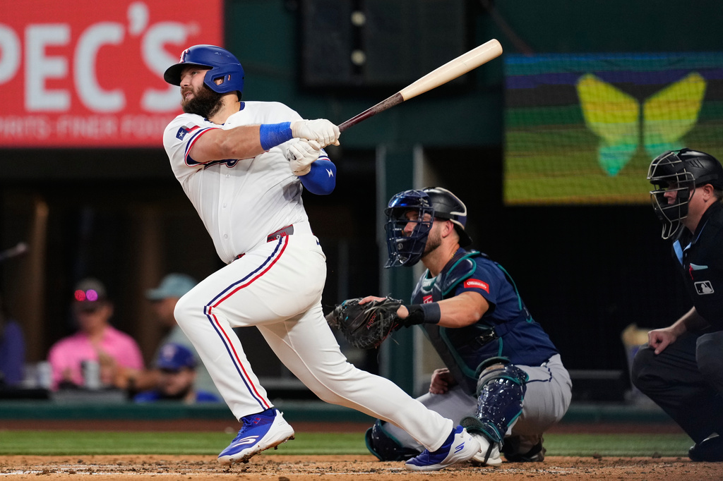 Texas Rangers' Jake Burger follows through on a two-run home run as Seattle Mariners catcher Mitch Garver and umpire Derek Thomas look on in the third inning of a baseball game in Arlington, Texas, Monday, July 27, 2026. (AP Photo/Tony Gutierrez)