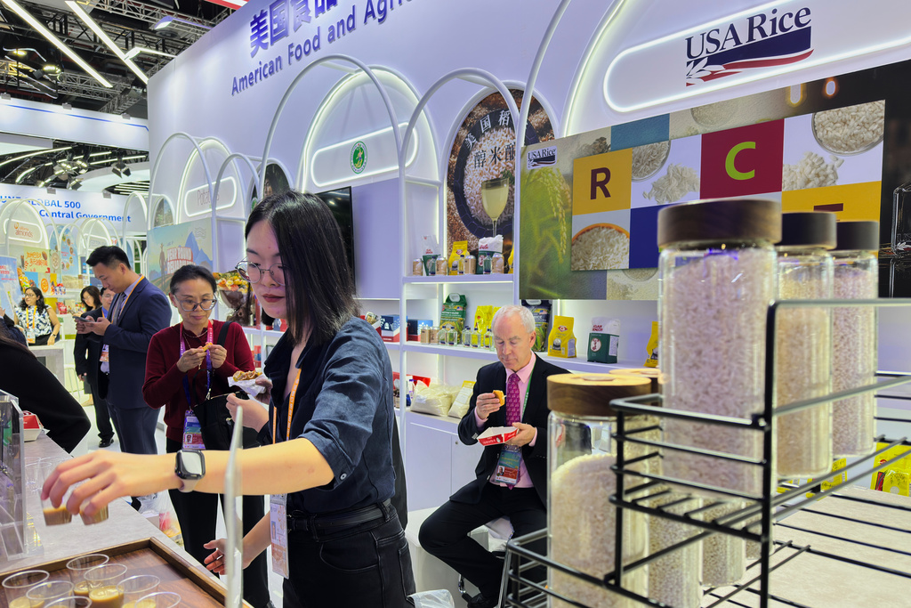 Visitors try out the snack foods and drinks made from rice at the exhibition booth of American Food and Agriculture during the China International Import Expo, in Shanghai, China, Thursday, Nov. 6, 2025. (AP Photo/Wayne Zhang)