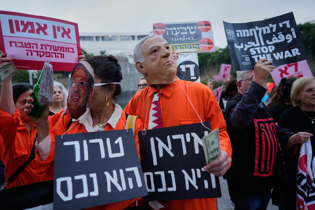 People dressed in orange prison jumpsuits and wearing masks of Israel's Prime Minister Benjamin Netanyahu and National Security Minister Itamar Ben Gvir gather to demonstrate against the ongoing war with Iran, in Tel Aviv, Israel, Thursday, March 19, 2026. Boards read in Hebrew: "Iran is an asset" and "Terror is an asset. (AP Photo/Maya Levin)