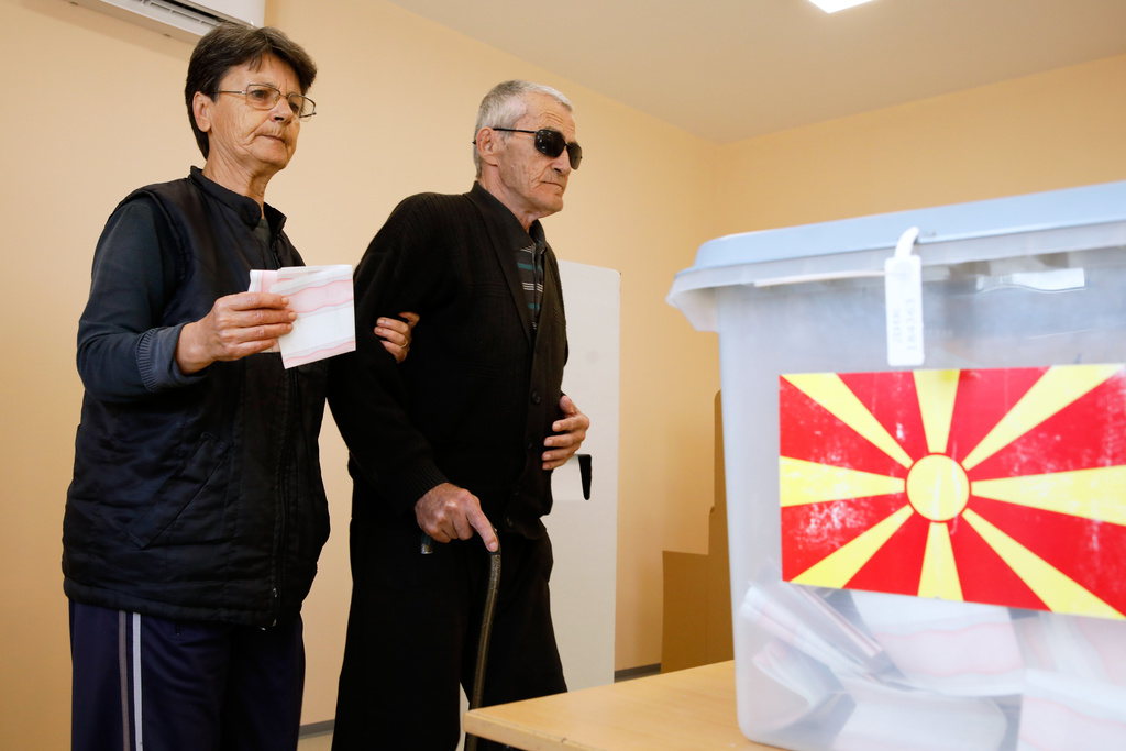 A woman holding ballots helps a man with impaired vision walk to the ballot boxes during the runoff local elections, at a polling station in Skopje, North Macedonia, on Sunday, Nov. 2, 2025. (AP Photo/Boris Grdanoski)