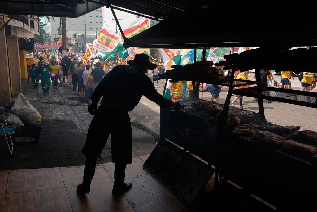 A vender cooks meat as a climate protest goes by during the COP30 U.N. Climate Summit, Saturday, Nov. 15, 2025, in Belem, Brazil. (AP Photo/Fernando Llano)