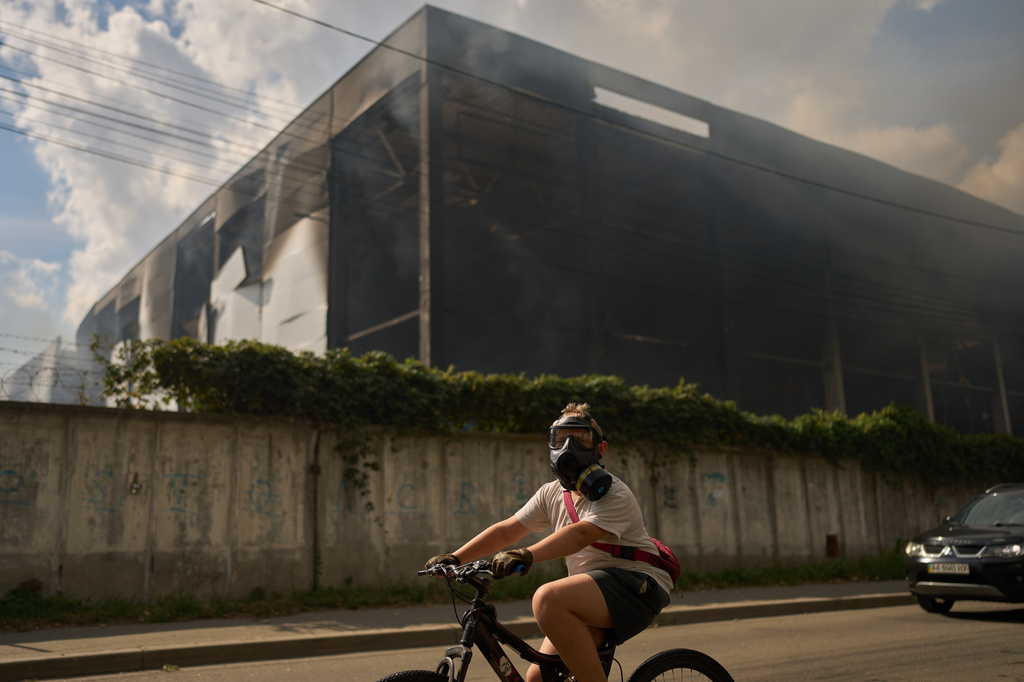 A local resident wears a gas mask as he rides a bicycle past a partially destroyed warehouse after a Russian drone attack in Brovary on the outskirts of Kyiv, Ukraine, Friday, Sept. 4, 2026. (AP Photo/Francisco Seco)