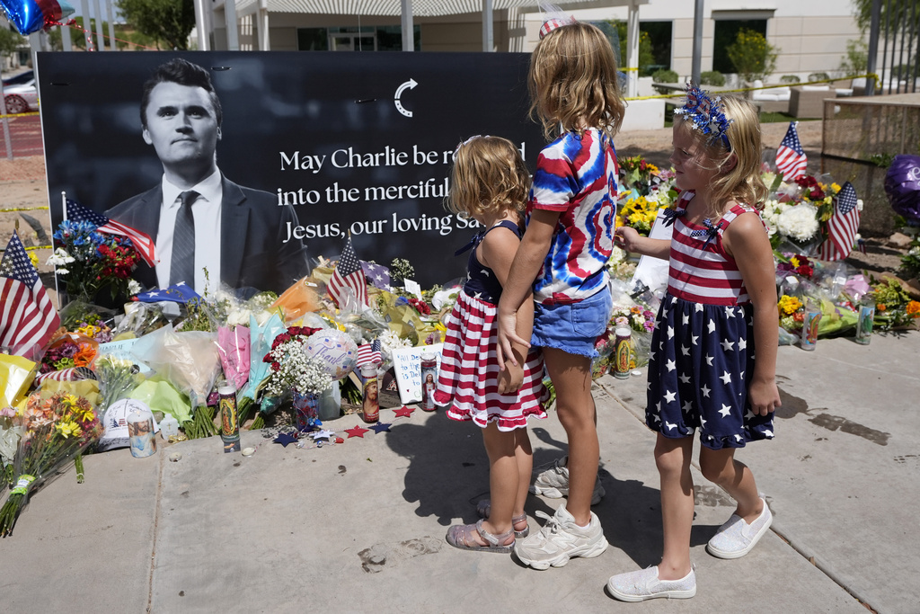 Sisters Clara Hetland, 4, left, Haddie Hetland, center, 9, and Audra Hetland 6, of Surprise, Ariz., spend time at a makeshift memorial set up at Turning Point USA headquarters after the shooting death at a Utah college on Wednesday of Charlie Kirk, the co-founder and CEO of the organization, Thursday, Sept. 11, 2025, in Phoenix. (AP Photo/Ross D. Franklin)