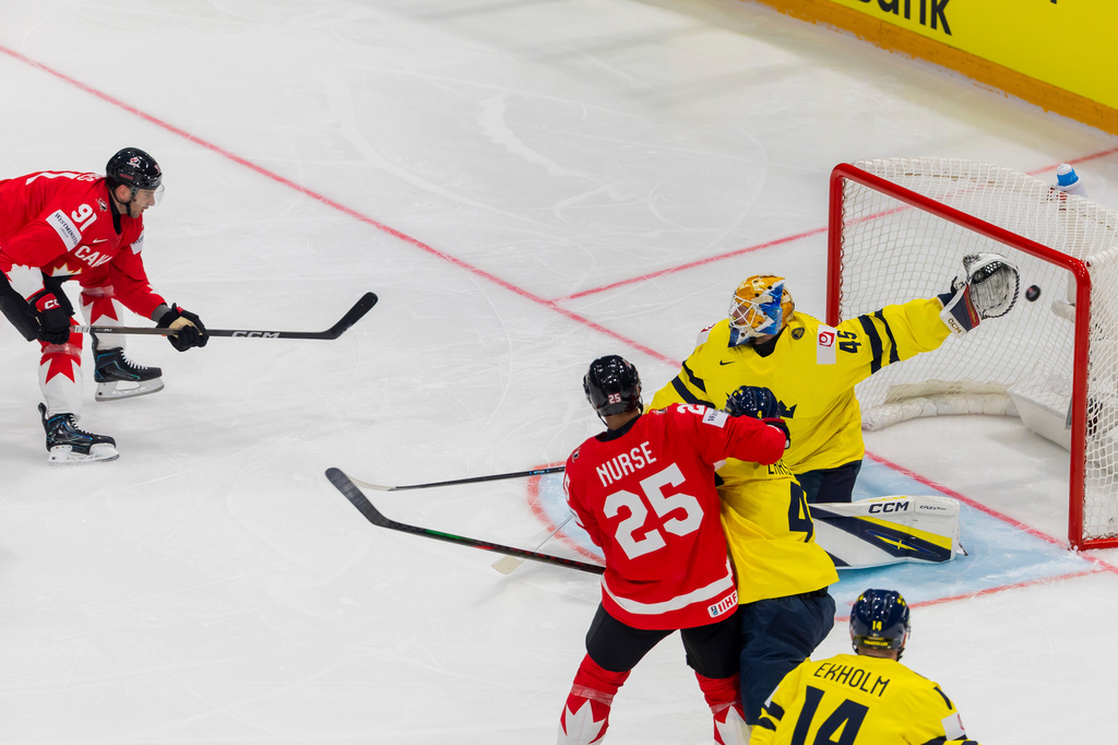 Canada's John Tavares, left, scores against Sweden goaltender Magnus Hellberg, during the 2026 IIHF Men's Ice Hockey World Championship preliminary round group B game between Canada and Sweden, at the BCF Arena ice hockey stadium, in Fribourg, Switzerland, Friday, May 15, 2026. (Salvatore Di Nolfi/Keystone via AP)