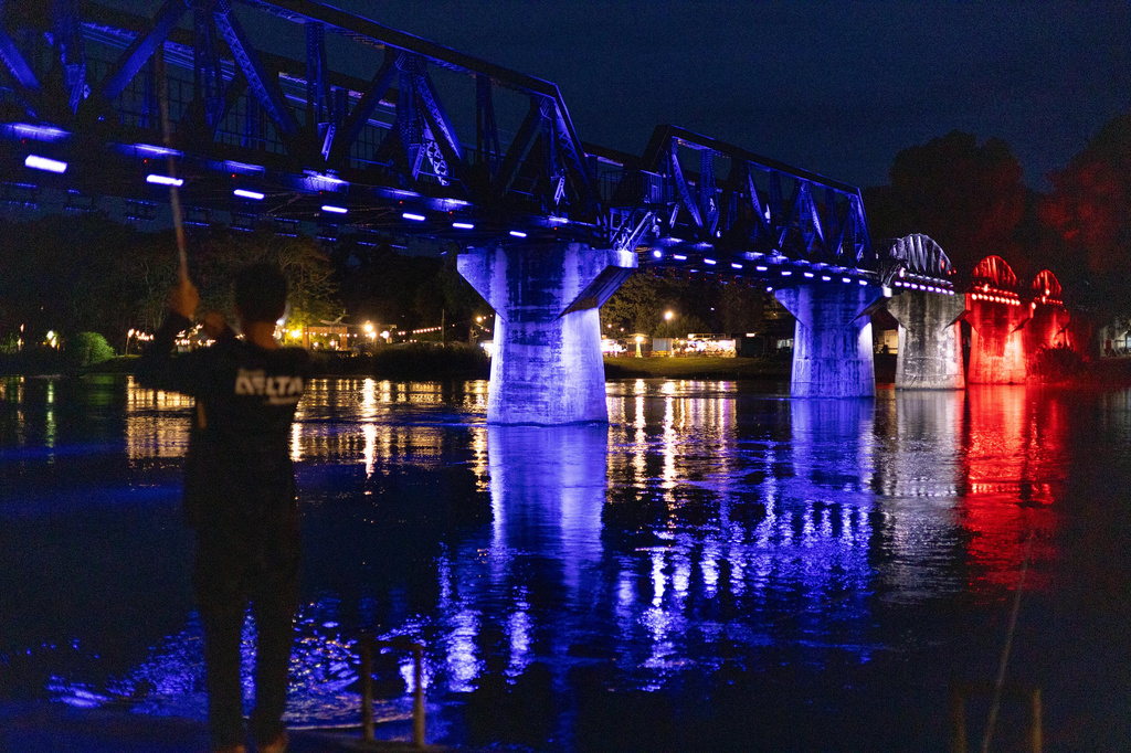 A man fishes in front of the River Kwai Bridge, one of the most iconic sections of the infamous World War II "Death Railway," as the bridge is lit up in the colors of the Thai flag in Kanchanaburi City, Thailand, Saturday, May 30, 2026. (AP Photo/Anton L. Delgado)