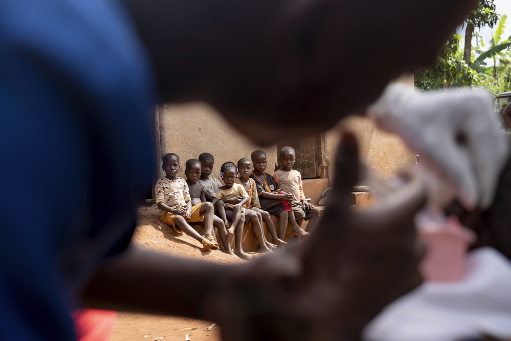 Neighborhood children watch as a nurse cleans the ear of an older resident on a visit by the NGO Reach One Touch Ministries, one of the few organizations in the country that care for older people, in Magogo, Uganda, Saturday, Nov. 16, 2024. (AP Photo/David Goldman)