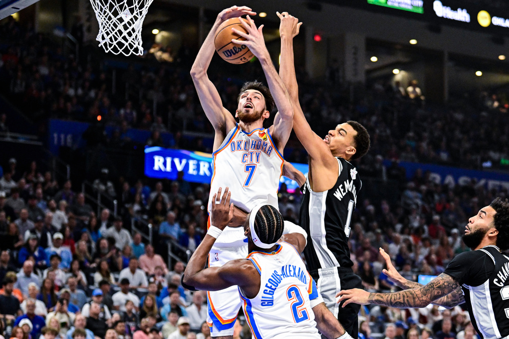 Oklahoma City Thunder Chet Holmgren (7) goes for the rebound against San Antonio Spurs forward/center Victor Wembanyama (1) during the first half of an NBA basketball game, Thursday, Dec. 25, 2025, in Oklahoma City. (AP Photo/Gerald Leong)