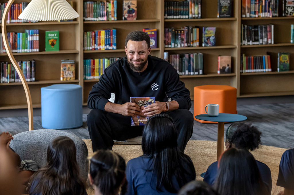 Warriors star Stephen Curry reads from the book, "Eye on the Ball" with students in the library during an event for his Eat.Learn.Play. Foundation at Madison Park Academy Primary in Oakland, Calif., on Wednesday, Sept. 23, 2026. (Carlos Avila Gonzalez/San Francisco Chronicle via AP)