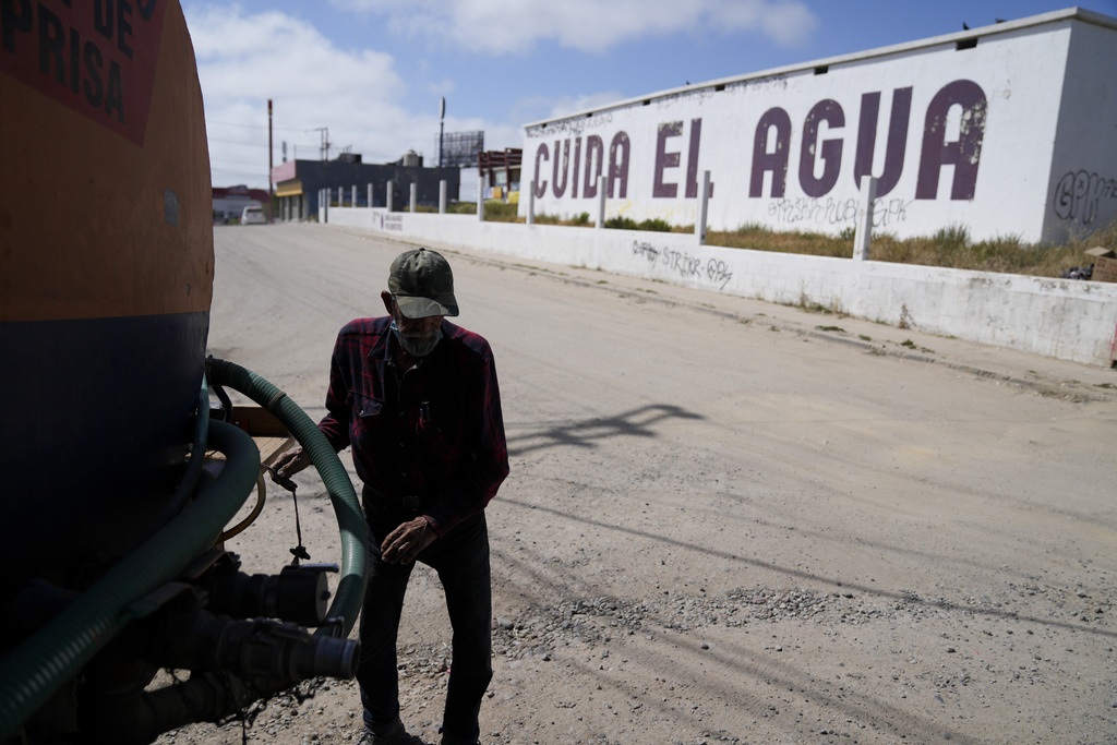 FILE - Augustin Rodriguez gets hoses ready on the back of his water truck as he delivers at a home across the street from a large sign that reads "conserve water," in Spanish, May 9, 2023, in Tijuana, Mexico. (AP Photo/Gregory Bull, File)