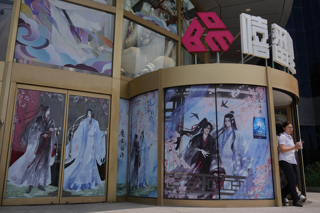 A woman walks out from a commercial office building entrance door displaying posters of the Boys' Love stories, in Beijing on July 14, 2025. (AP Photo/Andy Wong)