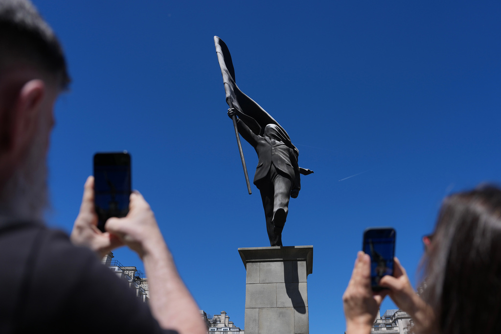 Members of the public look at a statue of a man holding a flag covering his face, and signed 'Banksy', which has appeared in Waterloo Place in London, Thursday, April 30, 2026. (AP Photo/Kin Cheung)